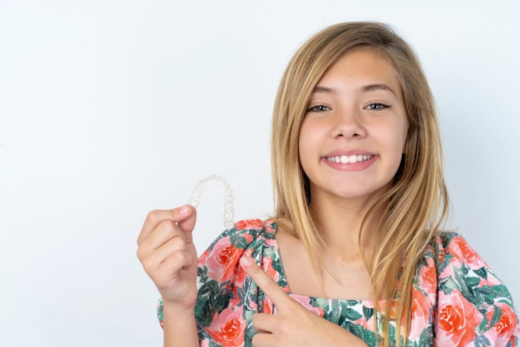 MODEL holding an invisible aligner and pointing at it. 