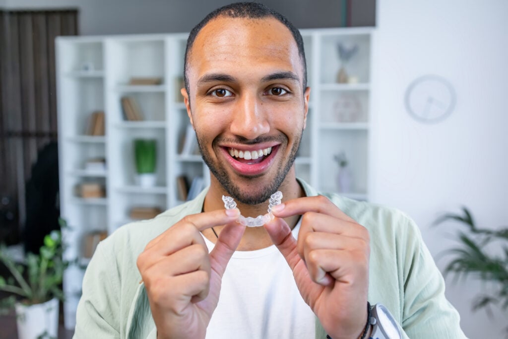 Adult man putting transparent braces for dental correction. holding invisible orthodontic retainer and aligner. Plastic braces dentistry to straighten teeth